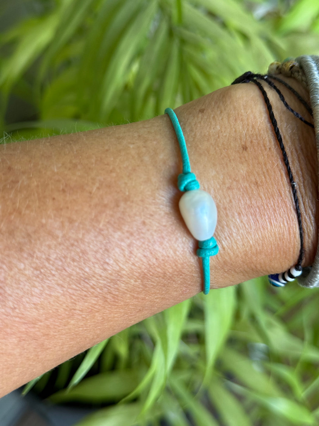 Close-up of a wrist wearing a green bracelet with a white pearl against a blurred green background